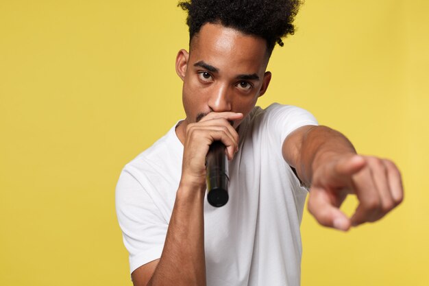 Stylish afro american man singing into microphone isolated on a yellow gold background