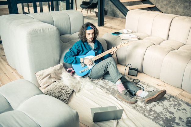 Stylish apartments. Calm young performer sitting on the floor and leaning new compositions while having opened laptop nearby