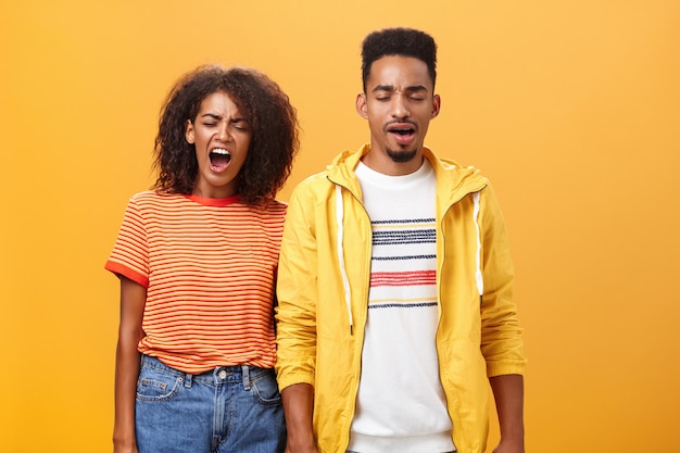 Stylish and attractive brother and sister over orange wall yawning with closed eyes and tired expression being drained and exhausted after dealing with house chores cleaning mess after party