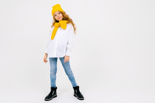 Stylish attractive caucasian girl in a white shirt and blue jeans and a yellow hat in boots posing on white studio full length with copy space