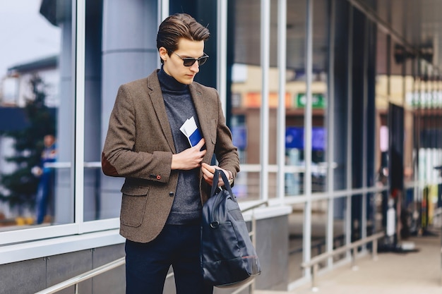 Stylish attractive guy in jacket with passport and tickets