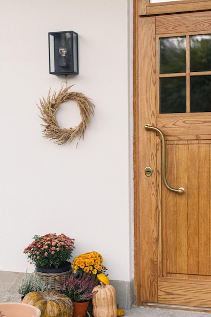 Photo stylish autumn decor of farmhouse entrance or porch autumn rustic wreath pumpkins and flower pots at front door fall arrangement