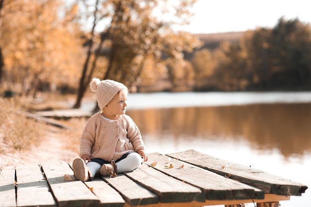 Stylish baby girl 1 year old wearing knitted autumn clothes sitting in park Looking away Childhood