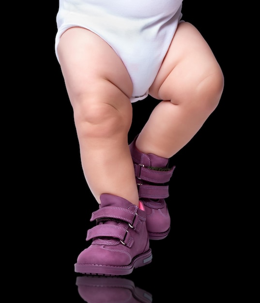 The stylish baby goes in boots. is isolated on a black background