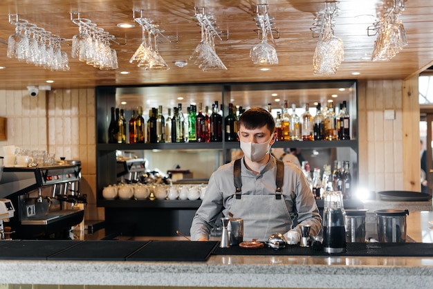 A stylish bartender in a mask and uniform during a pandemic is preparing cocktails at a party The work of restaurants and cafes during the pandemic