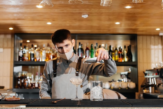 A stylish bartender in a mask and uniform during a pandemic is preparing cocktails at a party The work of restaurants and cafes during the pandemic