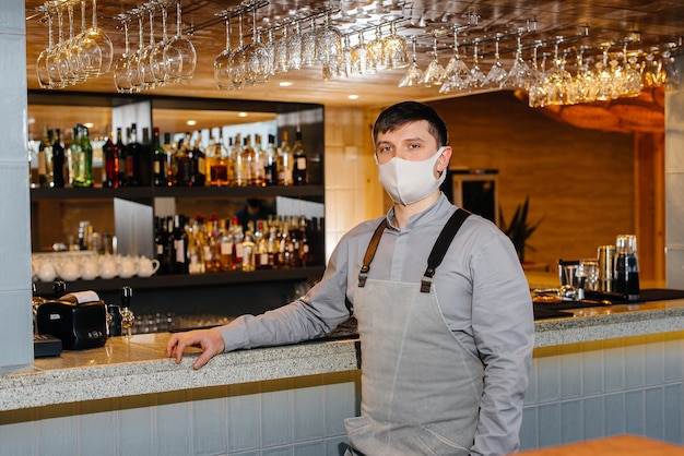 A stylish bartender in a mask and uniform during a pandemic. The work of restaurants and cafes during the pandemic.