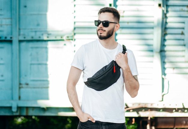 Stylish bearded hipster in the at the city in a white T-shirt with waist bag