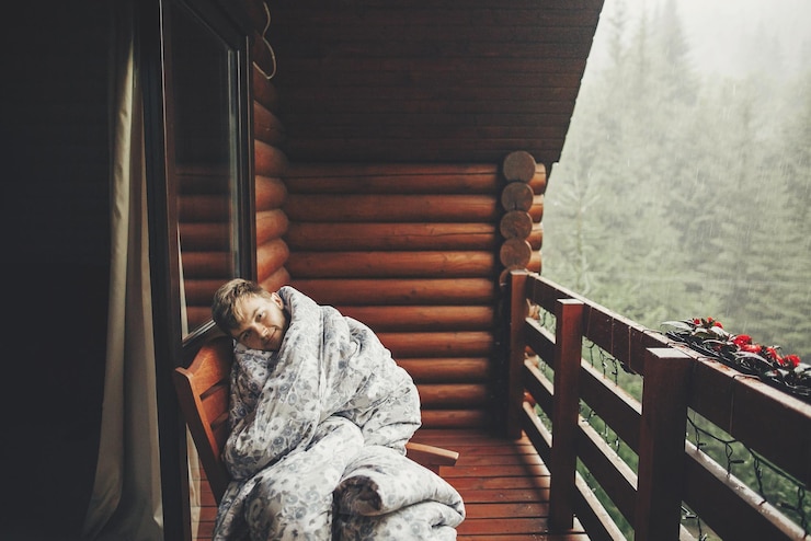 Photo stylish bearded man relaxing on wooden porch among forest in rainy mountains hipster guy resting in blanket sitting on cottage terrace while raining in woods calm peaceful moment
