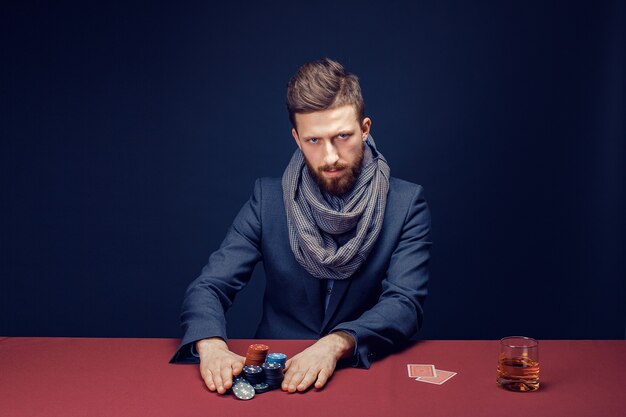 Foto elegante uomo barbuto in vestito e sciarpa che giocano nel casinò scuro