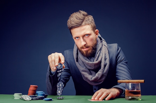 Стильный бородатый мужчина в костюме и шарфе, играя в темном казино