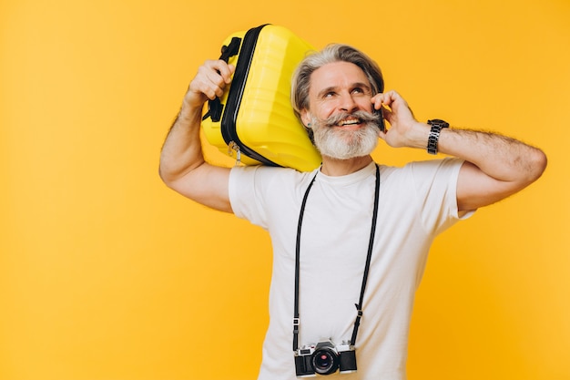 Stylish bearded man with camera laughing while holding a yellow suitcase chatting on phone