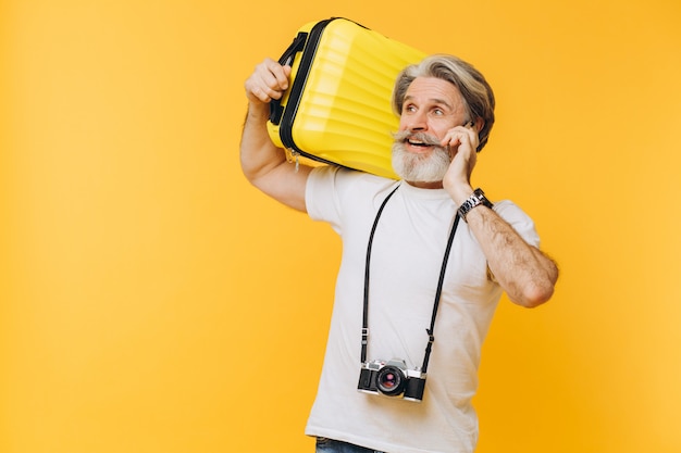 Stylish bearded man with camera laughing while holding a yellow suitcase chatting on phone