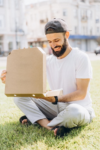 Stylish bearded man with a cardboard box of pizza place under your text or logo