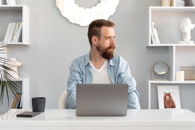 Stylish bearded man working on laptop from home sitting at the table