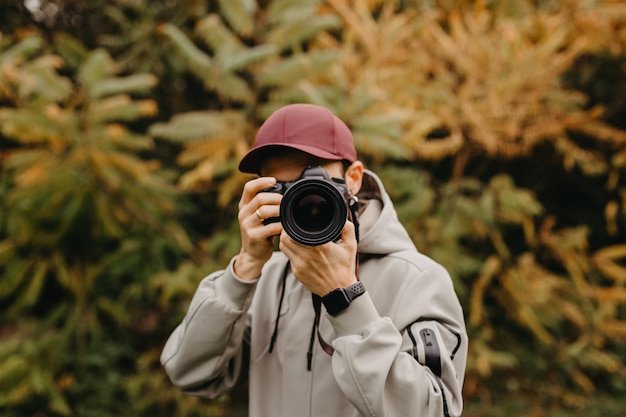 カメラを手にしたスタイリッシュなひげを生やした写真家が秋の公園で写真を撮る