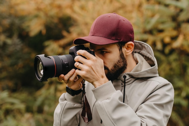 Photo stylish bearded photographer with a camera in his hands takes a photo in the autumn park