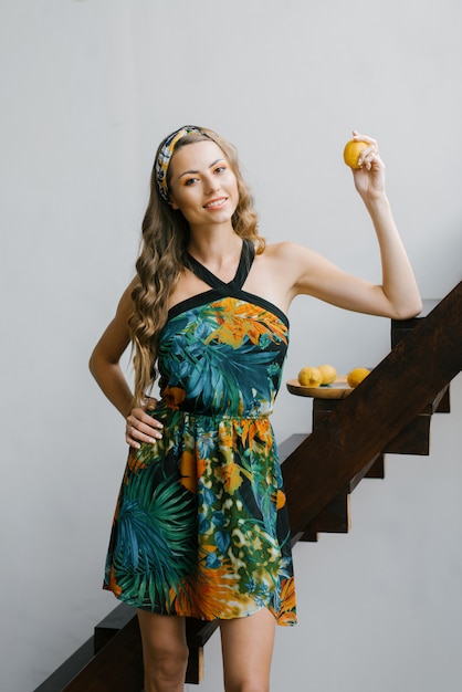 Stylish beautiful girl with professional makeup and curls in a sundress holding fresh organic lemons