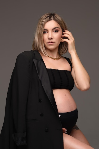 Стильная красивая беременная женщина сидит на стуле в куртке и держит руки на животе