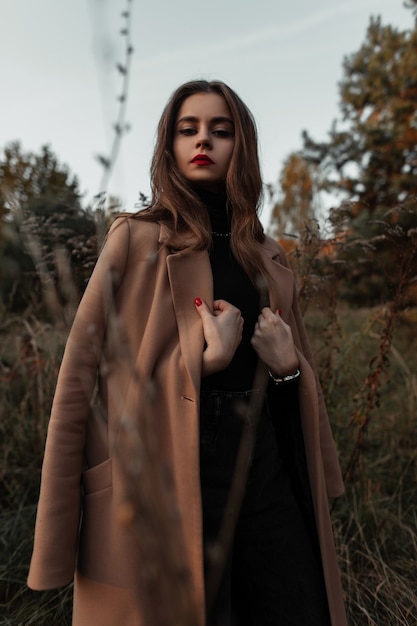 Stylish beautiful woman model in a fashion beige coat with black clothes in the grass on nature