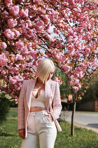 花の咲く桜の近くの公園で春の日にピンクの花でスタイリッシュで美しい女性