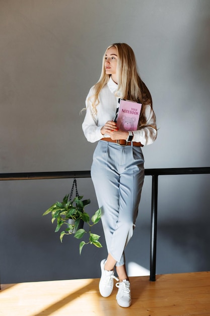 Stylish beautiful woman standing in the office holding a notebook