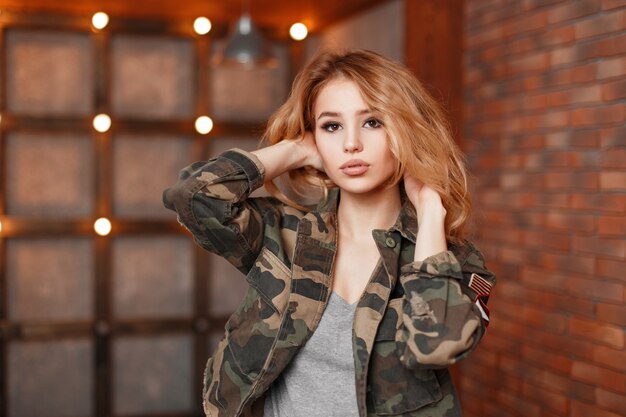 Stylish beautiful young woman in a fashionable jacket near wall with lights