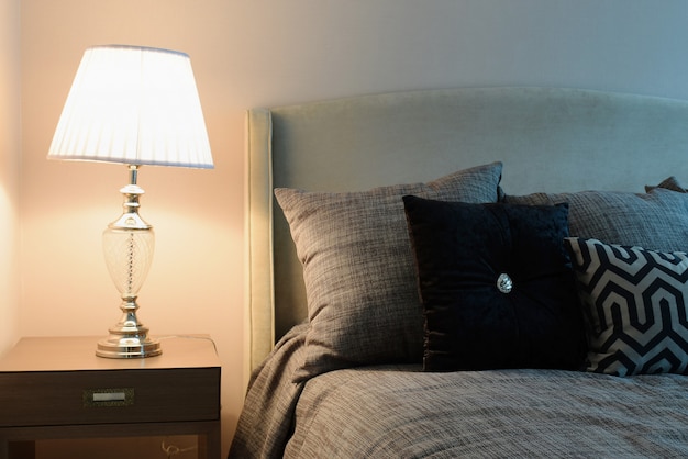 Stylish bedroom interior design with black patterned pillows on bed and decorative table lamp.