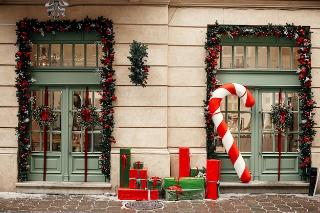 Stylish big candy cane red and green wrapped christmas gifts fir branches wreaths on building exterior Modern christmas decor in city street Winter holidays in Europe Merry Christmas