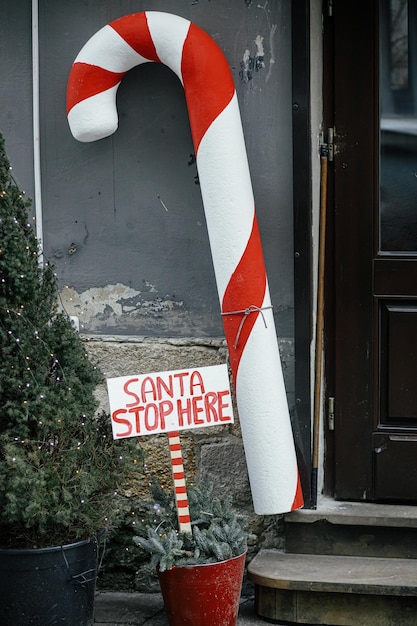 Stylish big candy cane and sign Santa stop here at building exterior Modern christmas decor in city street Winter holidays in Europe Festive decorations