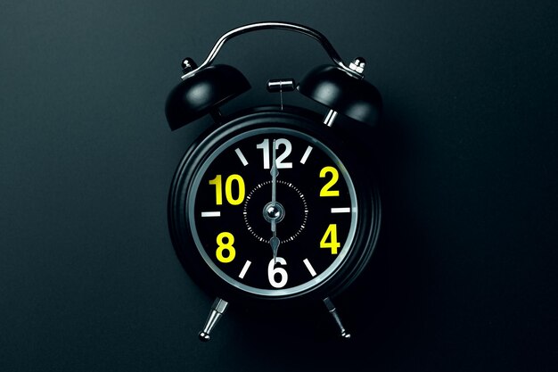 Photo a stylish black alarm clock with yellow and white numbers stands on a dark background blank for the designer