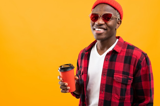 Stylish black american man in checkered red shirt with glass of coffee on yellow