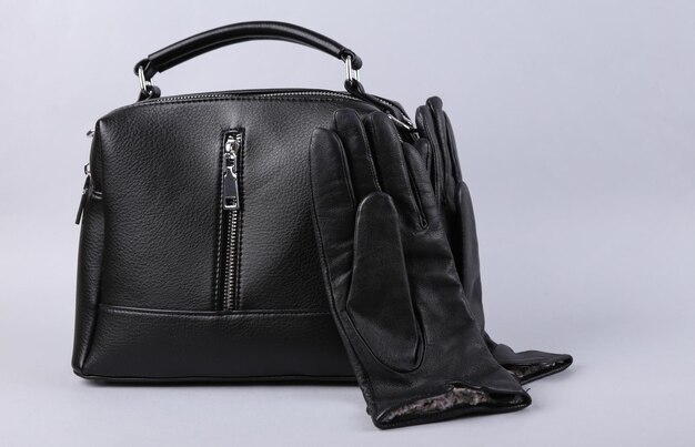 Stylish black leather gloves and handbag on gray background