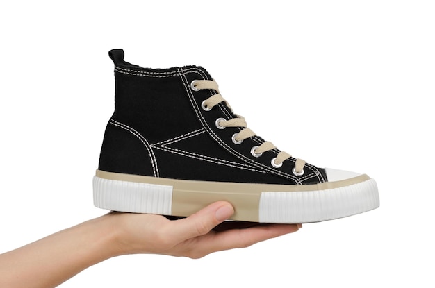 Stylish black sneaker in a female hand on a white background isolate