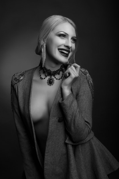 Stylish black and white studio portrait of a stunning woman with bright makeup wears jacket on a naked body