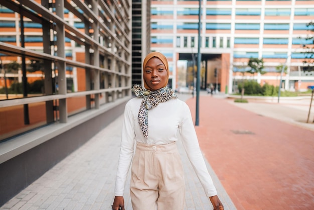 Stylish black woman in headscarf standing on street