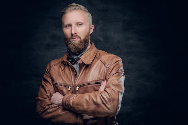 Stylish blond, bearded male with crossed arms, dressed in a brown leather pilot jacket.