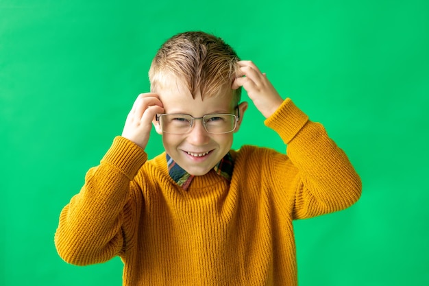 Stylish blond schoolage boy with an open book in his hands Cheerful boy in a yellow sweater and glasses on a green background isolate Back to school education learning the power of knowledge