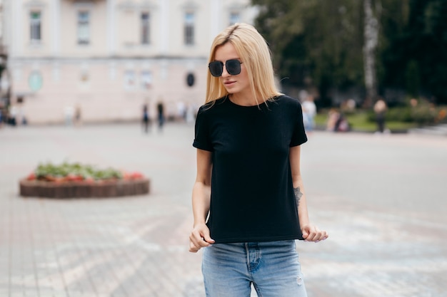 Stylish blonde girl wearing black t-shirt and glasses posing against street