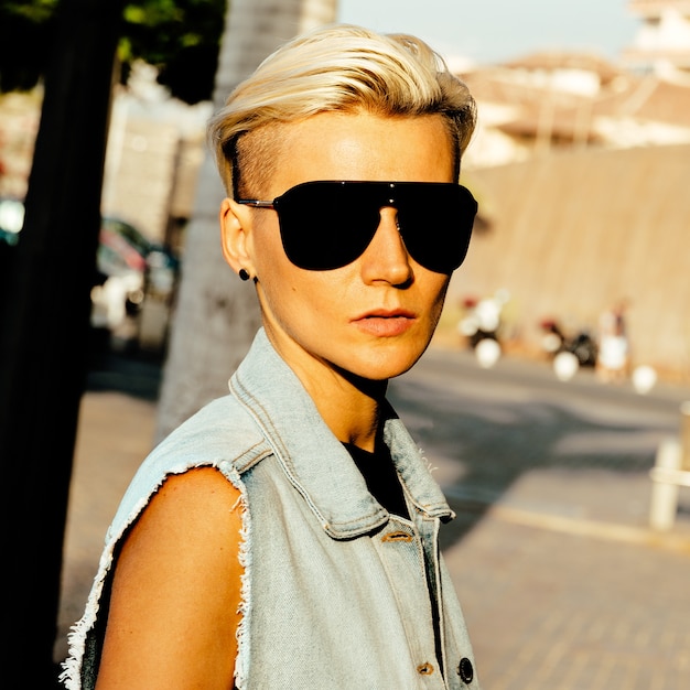 Stylish blonde in trend sunglasses and denim clothes in the city