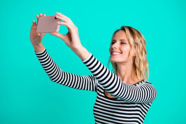 Stylish blonde woman in a striped sweater posing against the blue wall