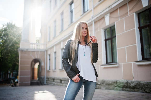 Stylish blonde woman wear at jeans, sunglasses and jacket posed at street on sunshine