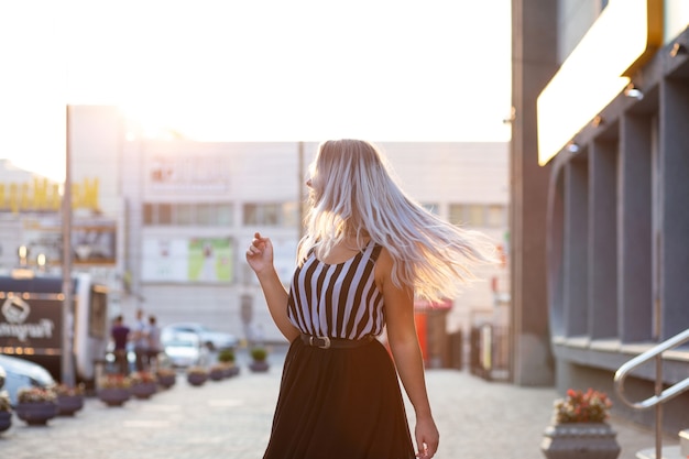 Stylish blonde woman with fluttering hair posing with evening light. Space for text