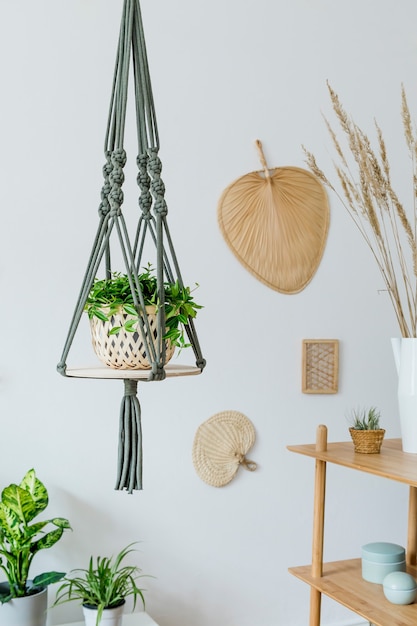 Stylish and boho home interior of open space with wooden desk, chair, lamp and white shelf.