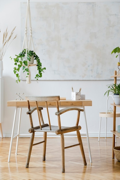 나무 책상 의자 램프와 흰색 선반이있는 작업 공간의 세련되고 boho 홈 인테리어 디자인 및 우아한 개인 액세서리 식물학 및 미니멀리즘 홈 데코 벽에 추상 그림