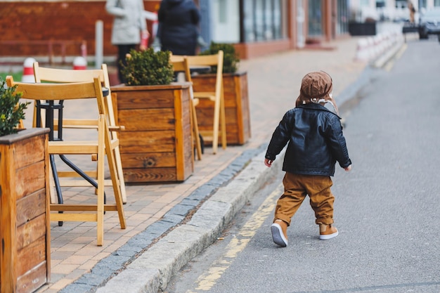 Stylish boy 3 years old in a leather jacket and brown trousers walks on the street Modern child Children's fashion Happy child