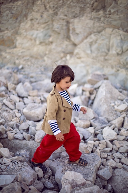 Stylish boy sailor in a vest and red pants sit at seashore