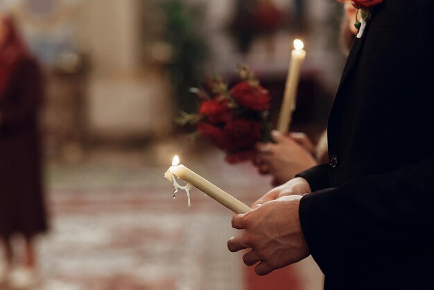 Фото Стильная невеста и жених, держащие свечи в руках на свадебной церемонии в церковной духовной паре, место для текста