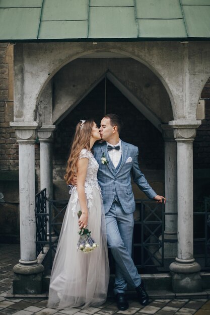 Stylish bride and groom kissing and embracing on background of old church Romantic moment