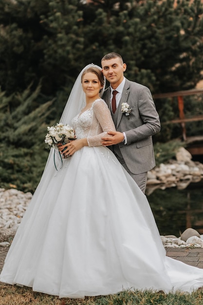 Stylish bride and groom tenderly embrace and kiss Beautiful bride with modern bouquet embracing stylish groom in autumn park Sensual romantic moment Wedding Stylish and beautiful